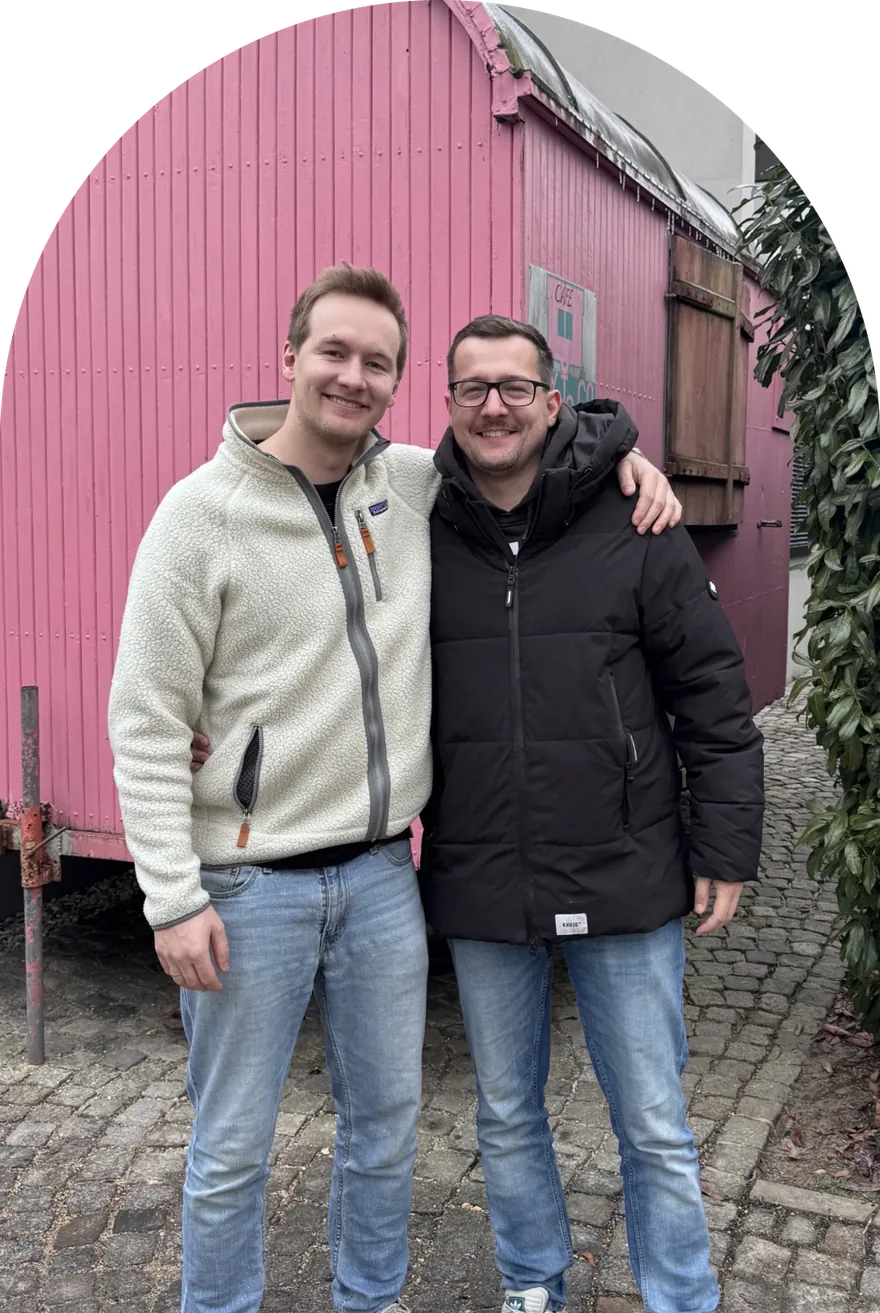 Die Spritzbuben – zwei Freunde Arm in Arm vor dem pinken Bauwagen